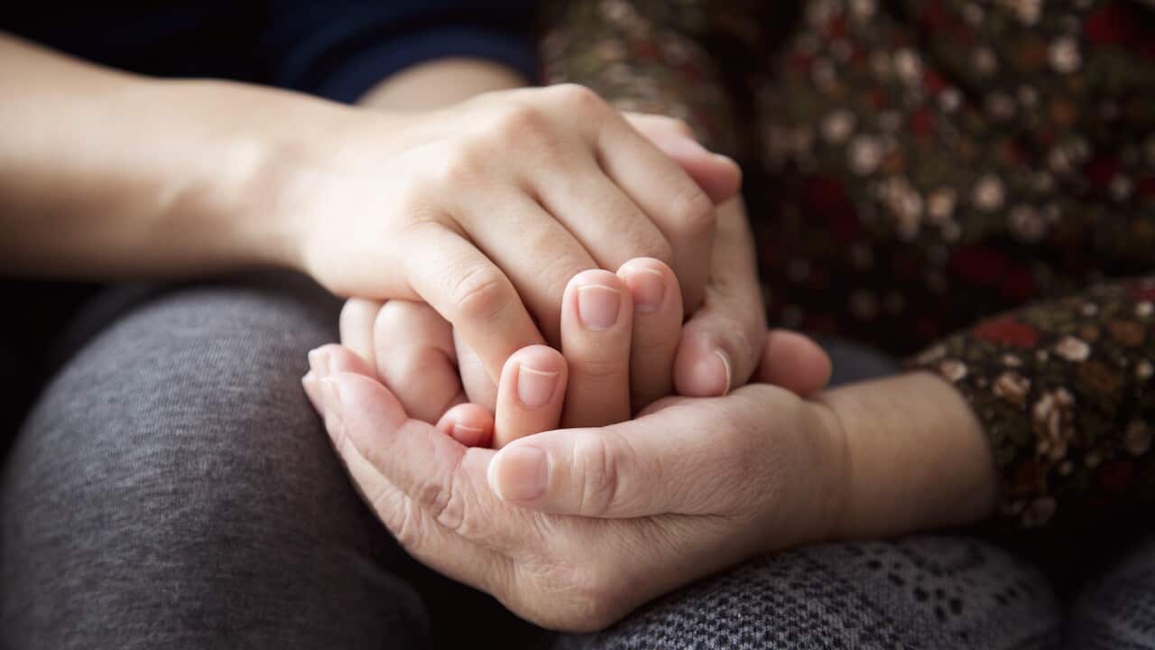 Hands of a senior woman and her daughter holding each other's hands together