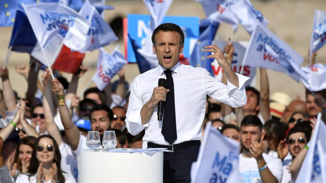 Emmanuel Macron addresses voters on his election campaign in front of many voters flying his party flag.