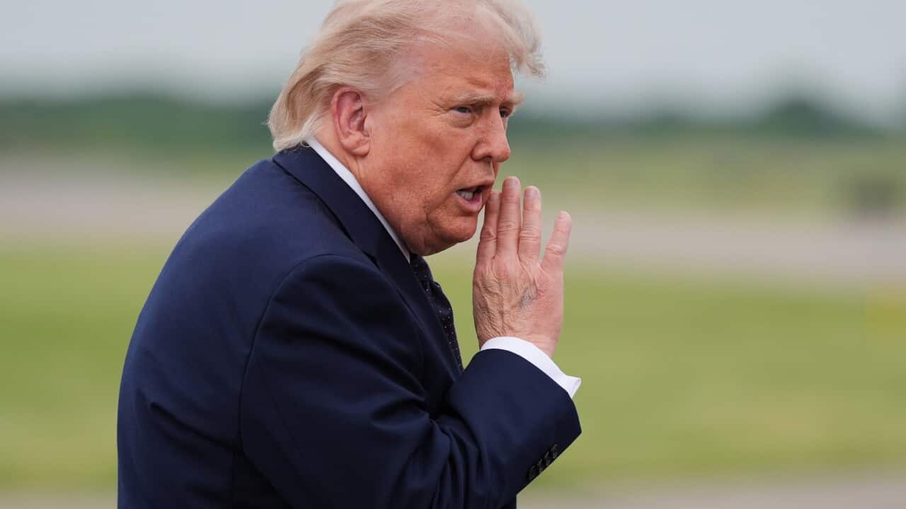 Trump sitting at his desk in the Oval Office at the White House wearing a navy suit and a red tie