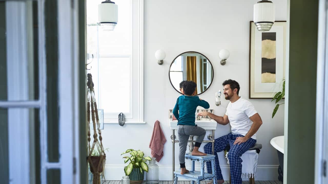 Father helping son brushing teeth in bathroom
