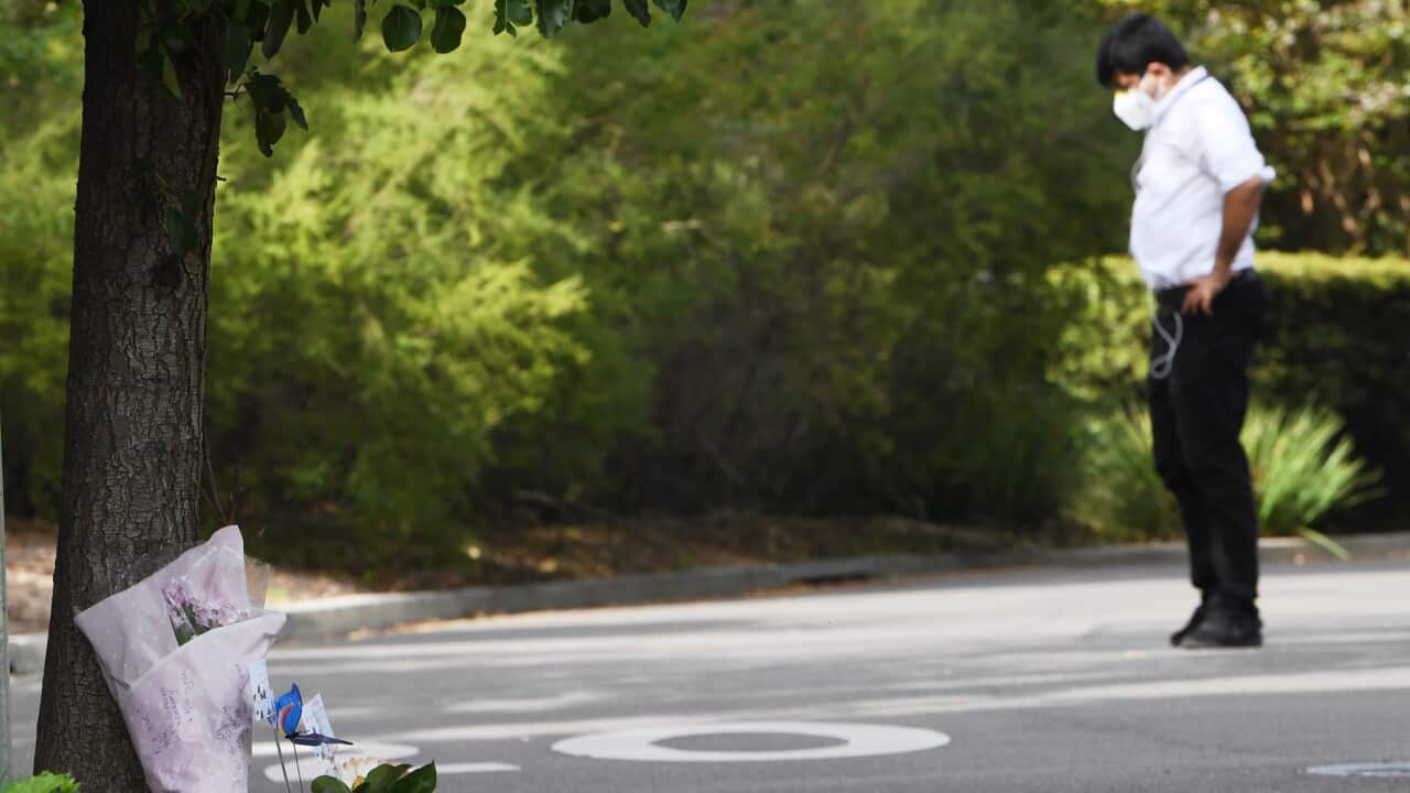 A security guard stands in the driveway as flowers are seen left at the entrance to Anglicare Newmarch House aged care home.