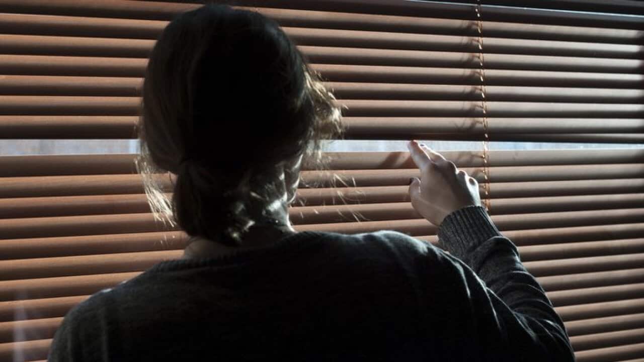 A woman looks out a window through a blind. Picture posed by model - model release available..
