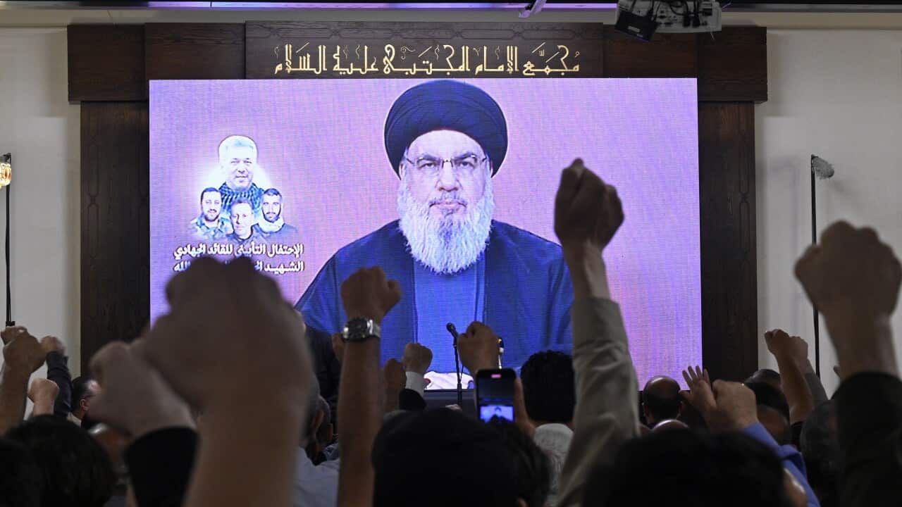 A crowd of people watching a broadcast address by Hezbollah leader Hassan Nasrallah raise their fists in the air.