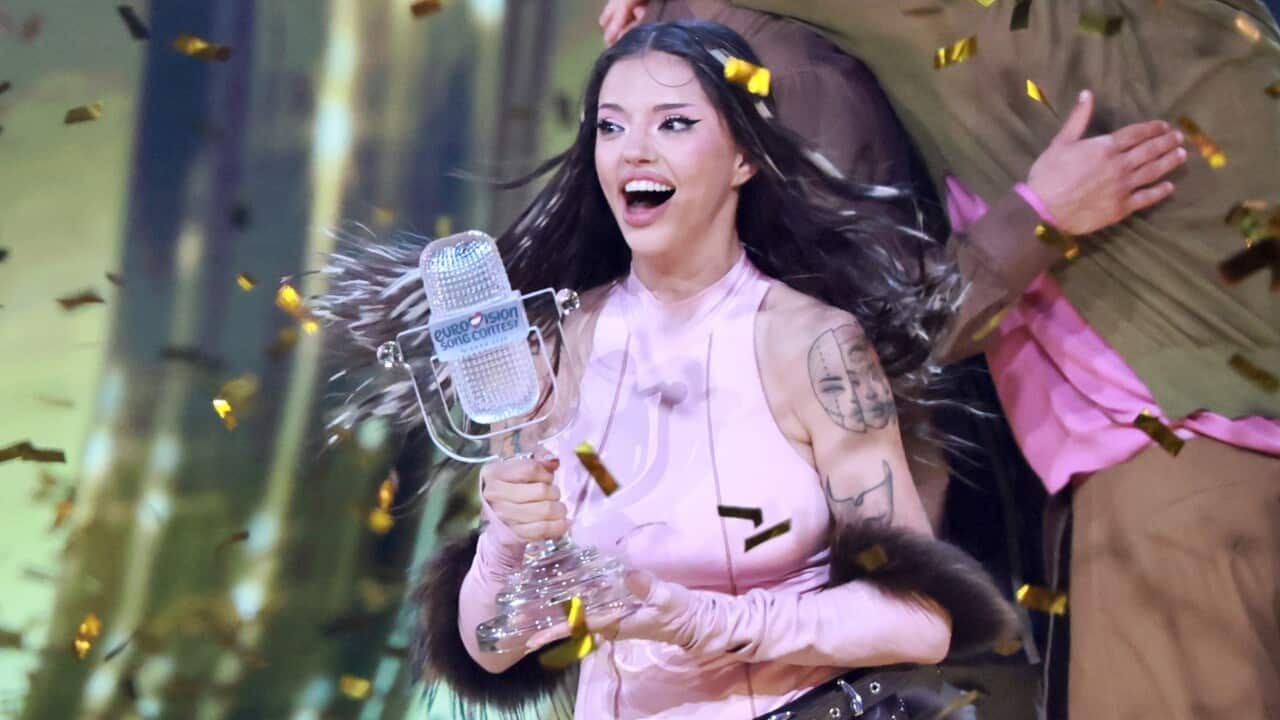 A smiling dark haired woman in a pink top accepts an award as confetti sprays around her.