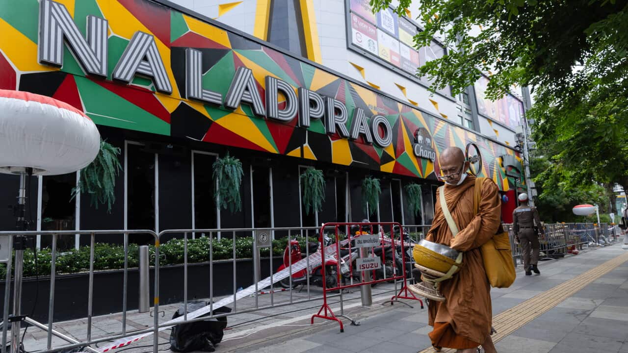 A monk in orange robes walks past a fenced off pub in Thailand