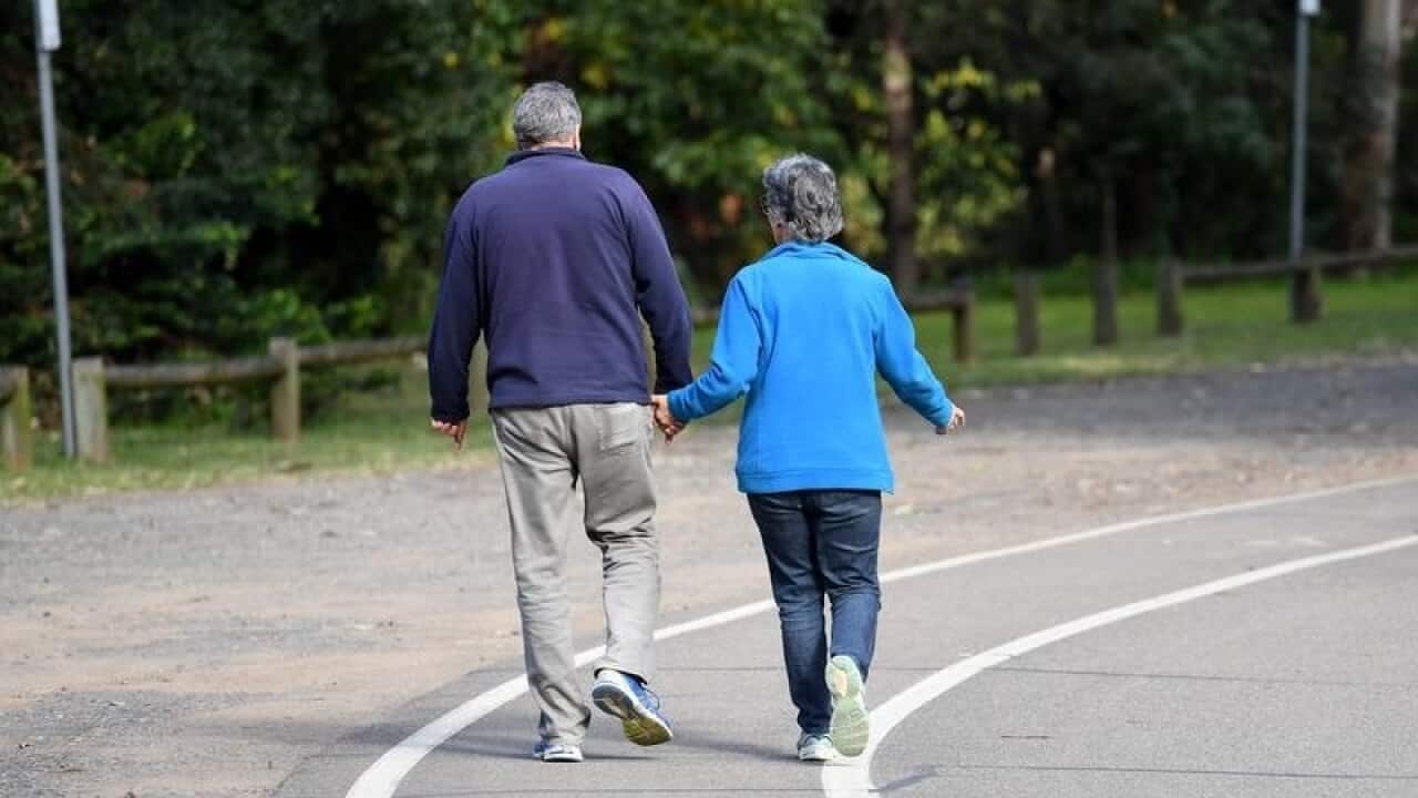 An elderly couple walk through a park
