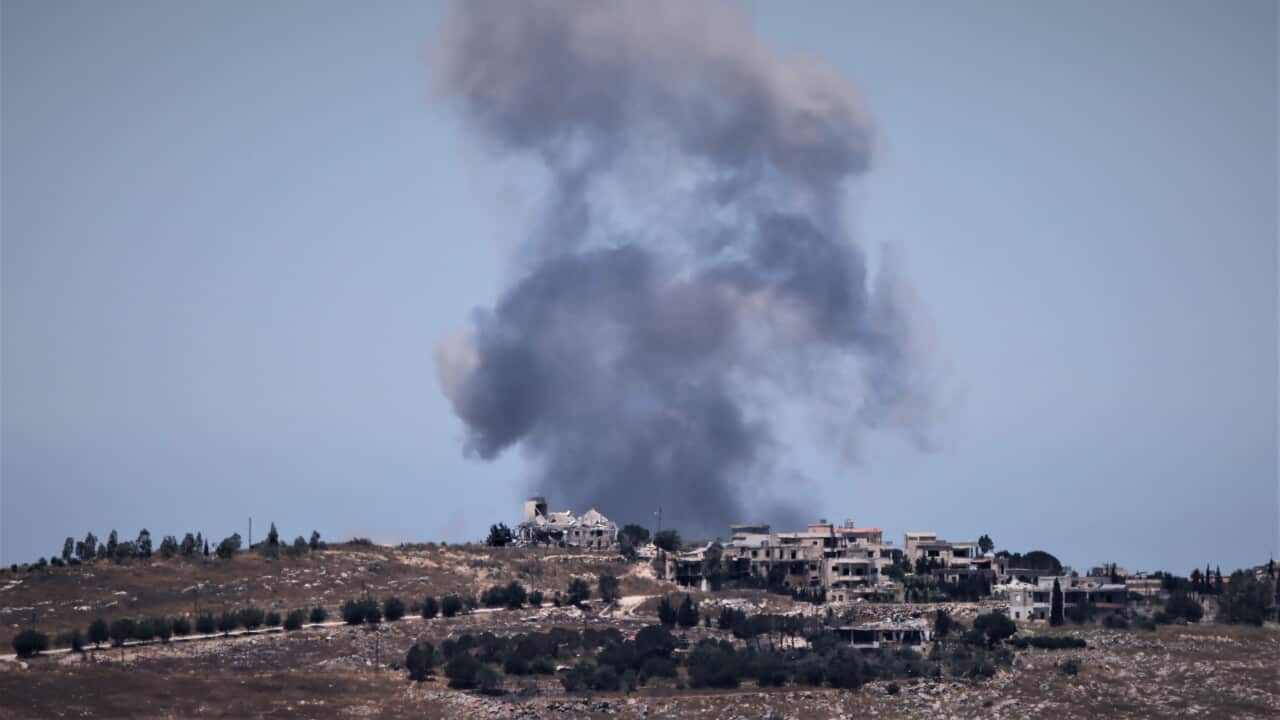 Smoke rises over buildings on rocky terrain.