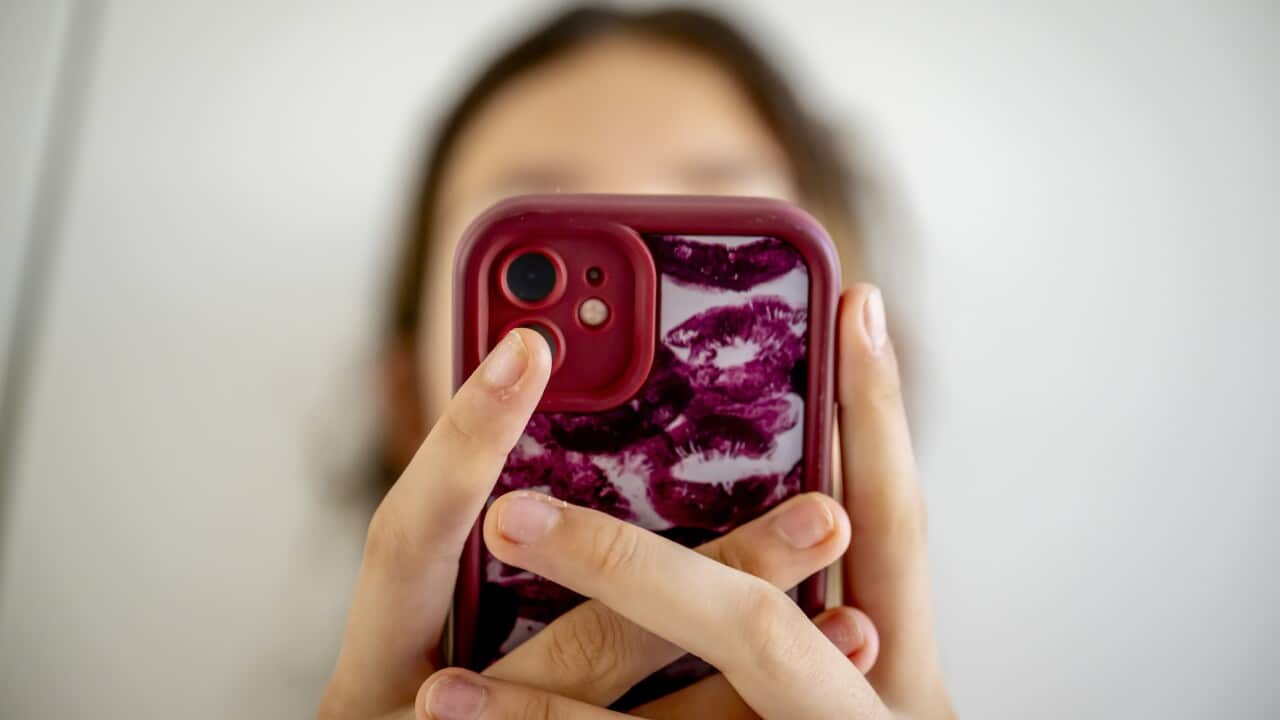 A close up shot of a young woman looking at her phone with a red case.