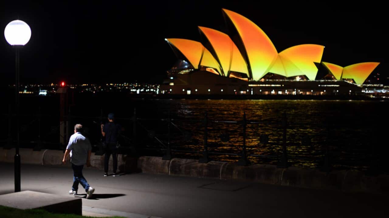People walk past the Opera House while it is lit up in a gold colour to mark the start of the Diwali Hindu festival in Sydney