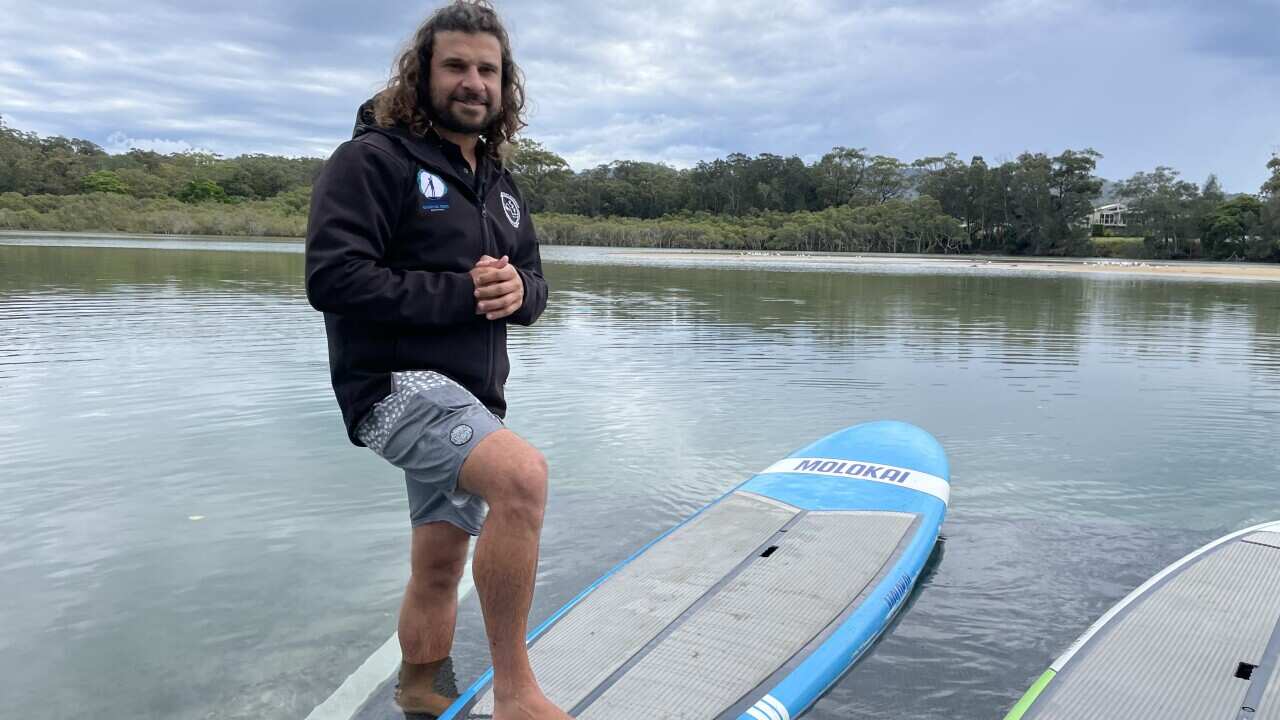 Clark Webb carries a paddleboard from the water at Coffs Creek