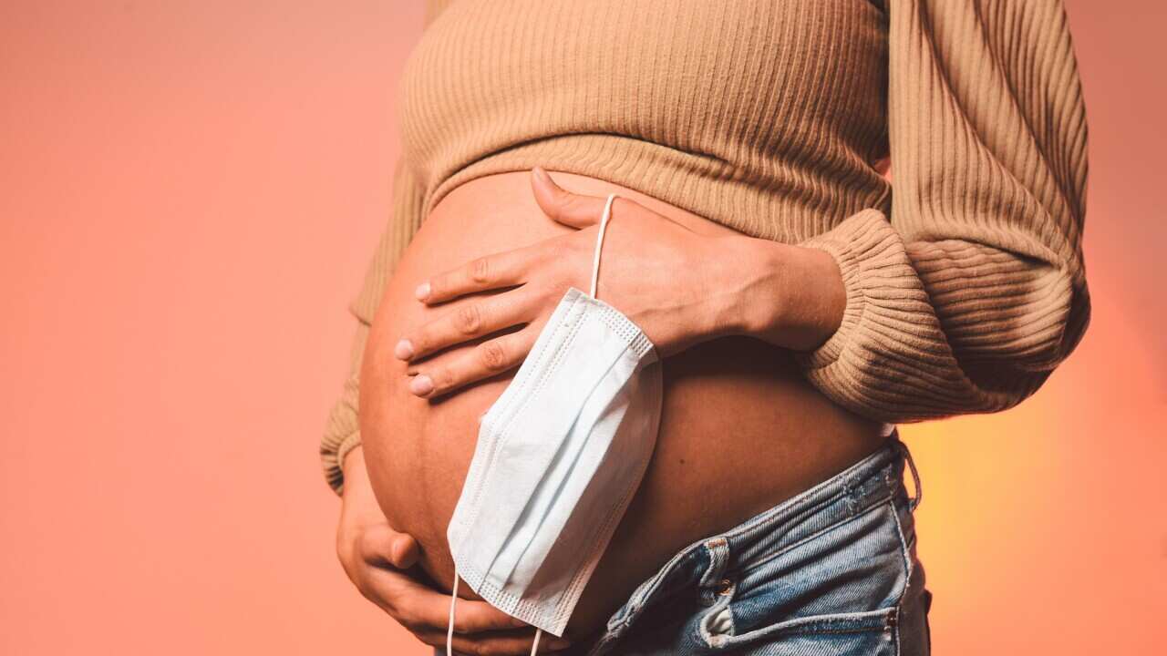A pregnant woman holds a mask