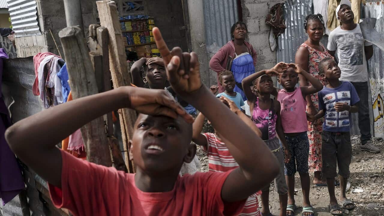 Locals look up to a helicopter bringing aid to earthquake victims