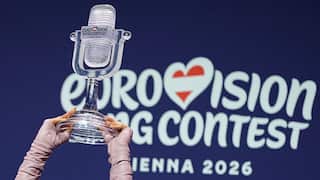 A pair of gloved hands hold a glass microphone trophy aloft in front of a blue sign with white writing.
