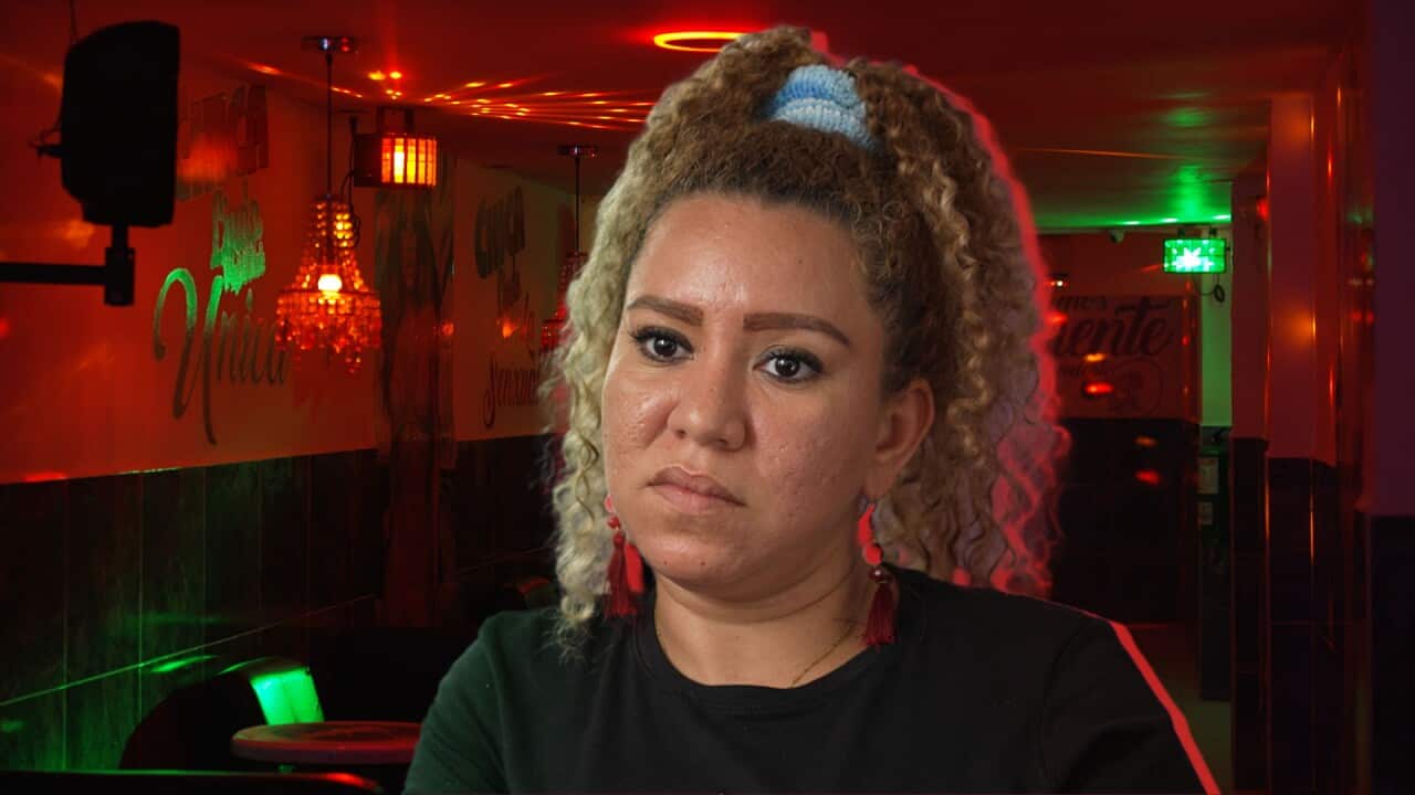 A headshot of a woman with curly blonde hair tied in a high ponytail. She is wearing a black t-shirt