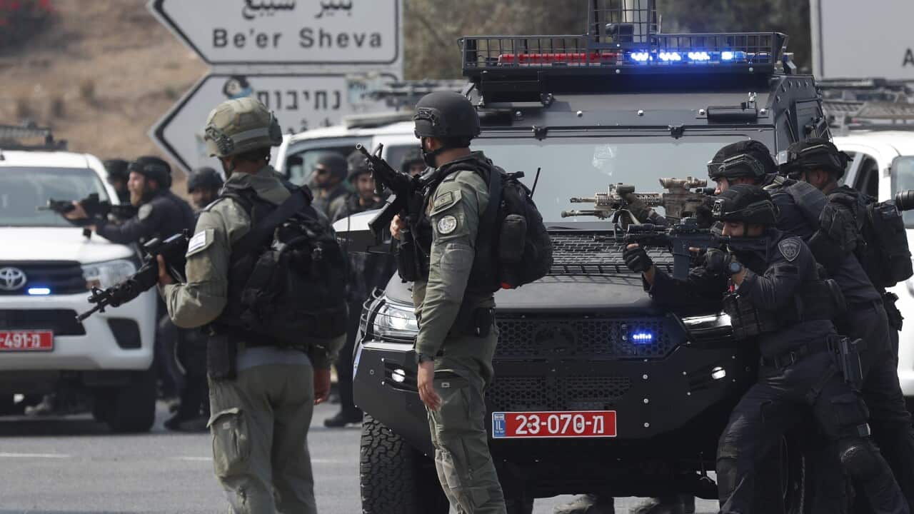 Israeli soldiers stand next to parked vehicles with their guns aimed.