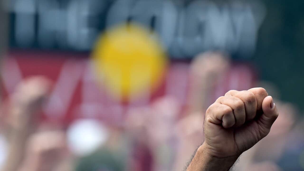 A closed fist is held in the air in front of a crowd holding signs.