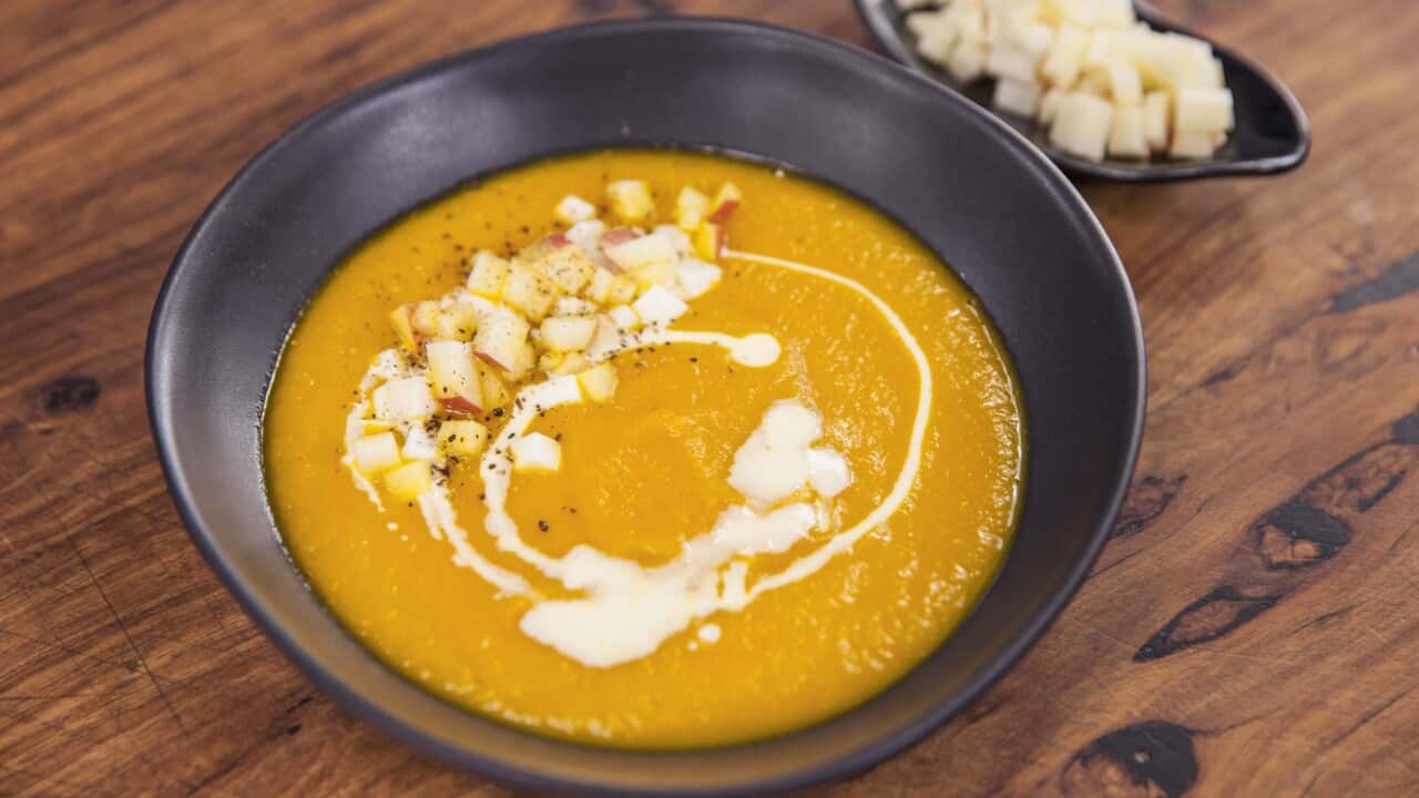 A vibrant orange soup sits in a brown bowl.