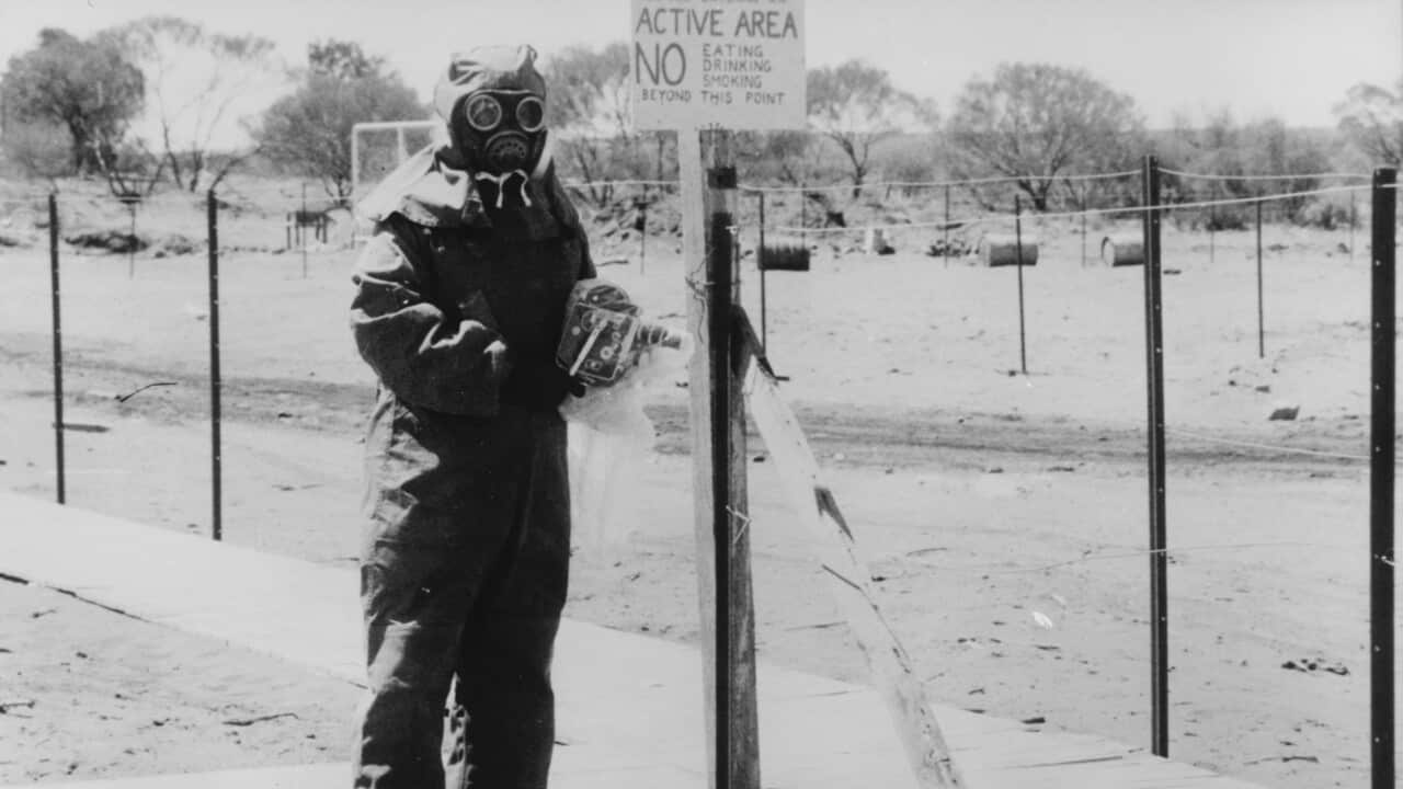 Black and white image of a person in a hazmat suit and gas mask in front of a radioactive zone at Maralinga.