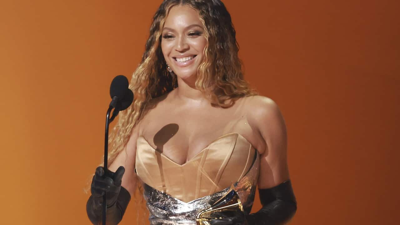A woman holding a trophy while standing on stage and speaking in front of a microphone.