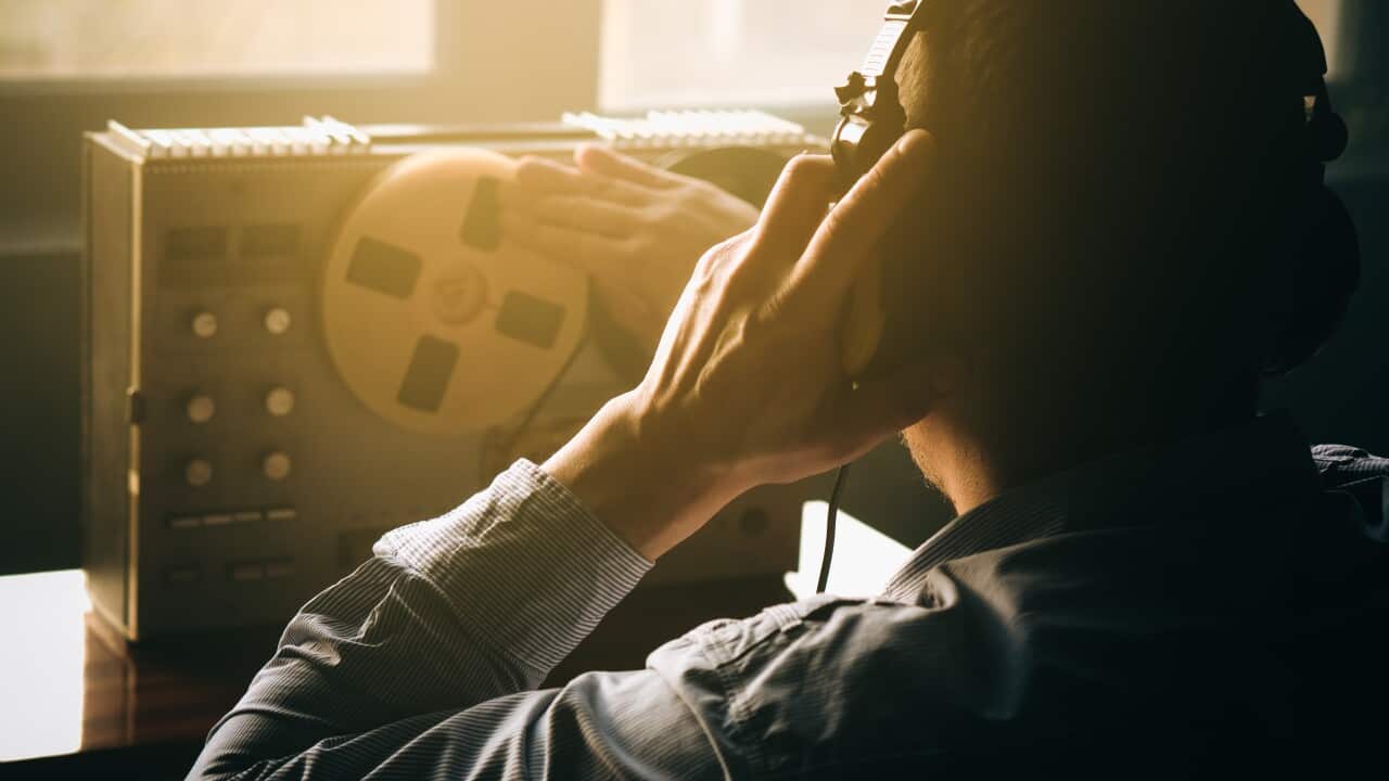 A man listens with headphones to a reel tape recorder