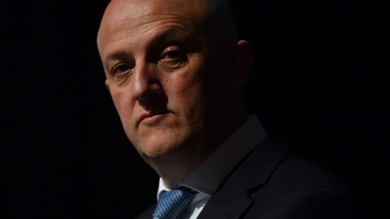 Man in suit looks into the camera in partial darkness.