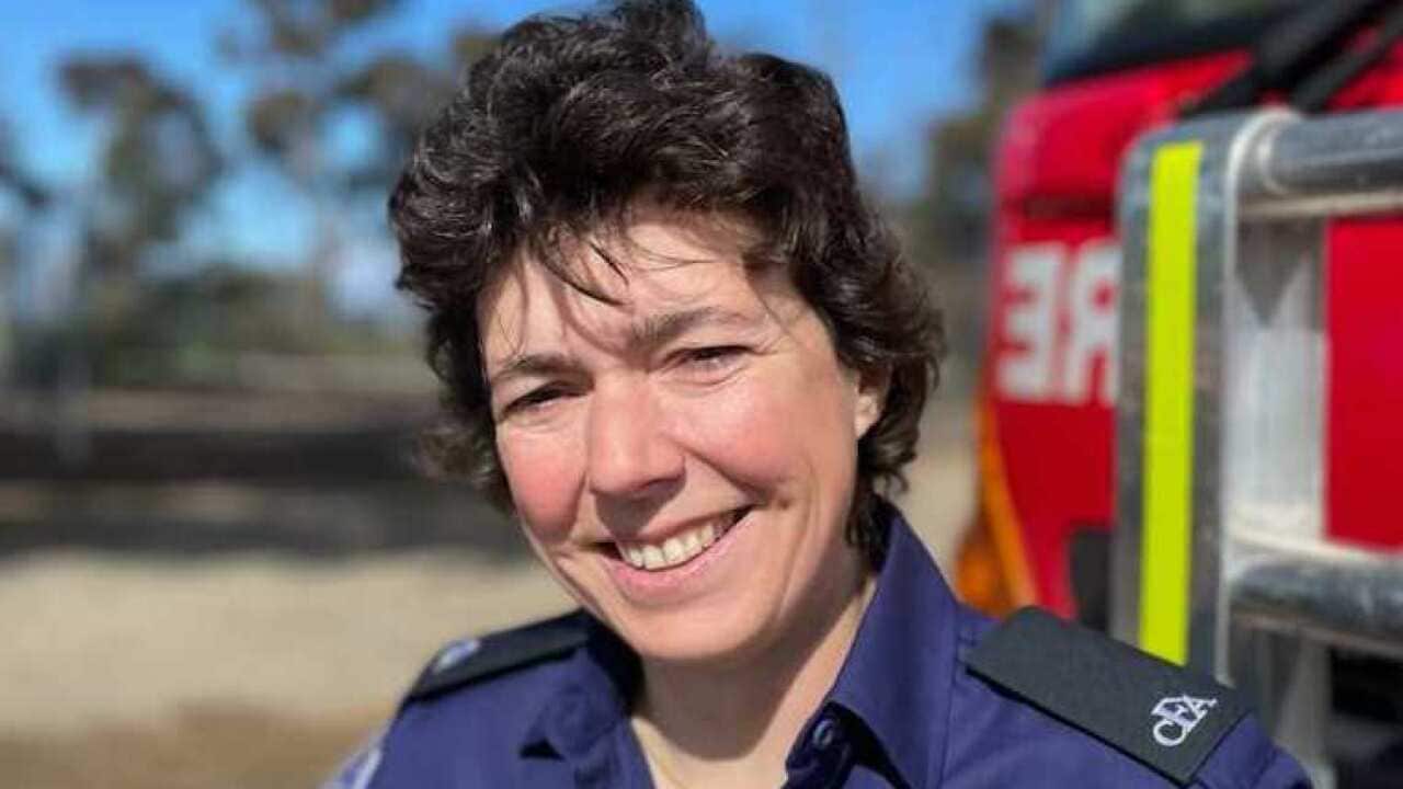 A woman dressed in a blue uniform stands in front of a red fire truck