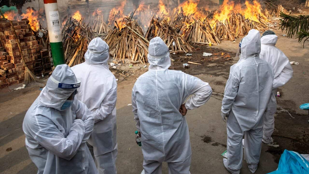 Visitors dressed in PPE suits watch as bodies are collectively lit at the converted parking lot of the Gazhipur cremation ground in New Delhi, India on April 28, 2021. A massive spike in Covid-19 cases and consequent deaths have overwhelmed the cremation