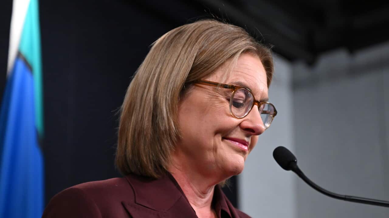 Jacinta Allan in a burgundy suit gives a speech at a lectern with two Australian flags and one First Nations flag in the background