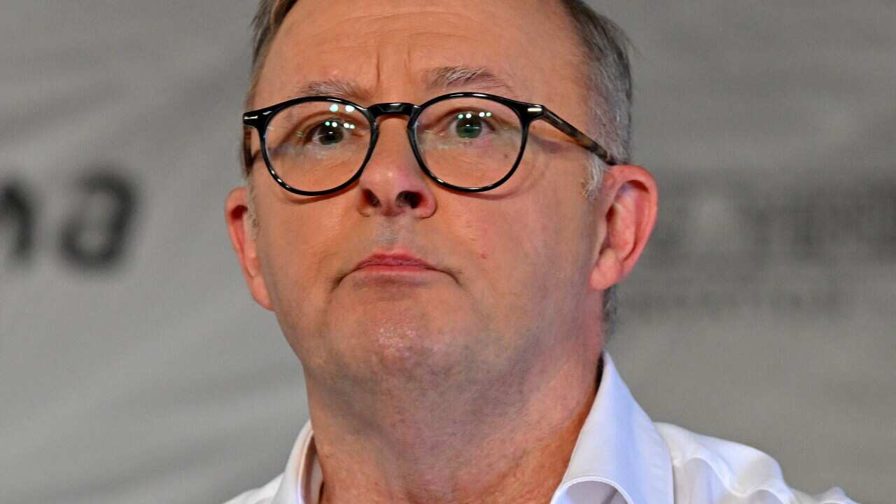 A man standing at a lectern speaking in front of microphones.