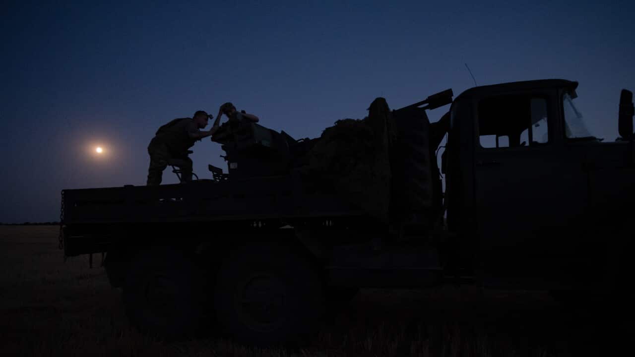 People standing on the back of an army vehicle at night in a field.