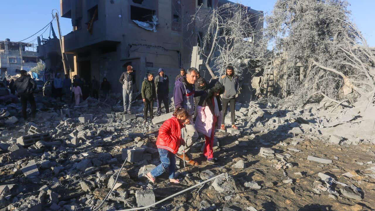 People including children walking among rubble.