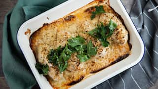 A vintage white baking tray holds a creamy chicken bake, topped wiht fresh herbs.