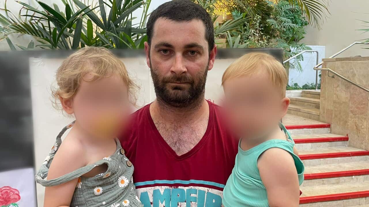 A man holding his two children and looking into the camera.