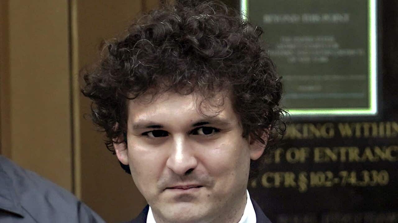 A man in a navy suit, white shirt and white and blue patterened tie outside a court room