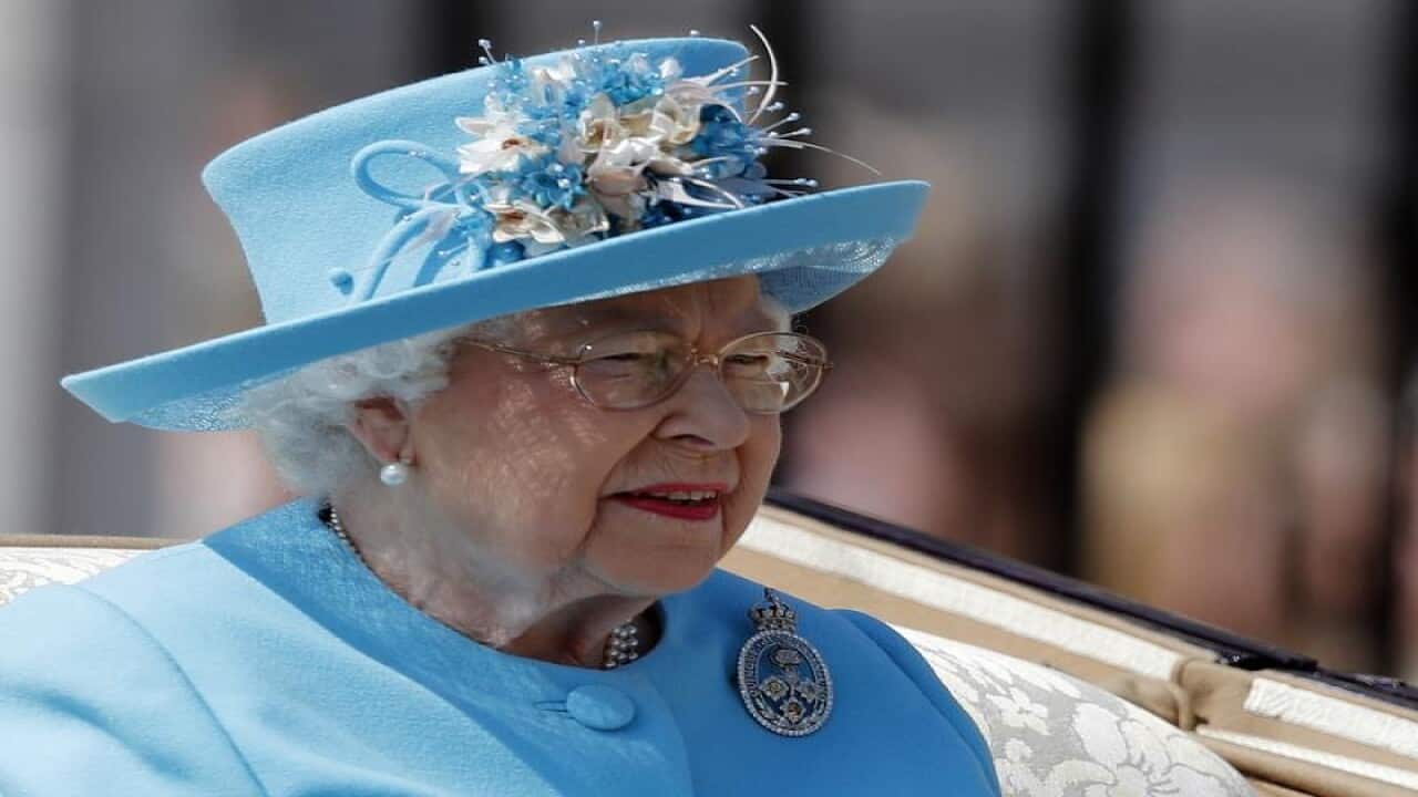 Queen Elizabeth in a blue hat riding in a carriage