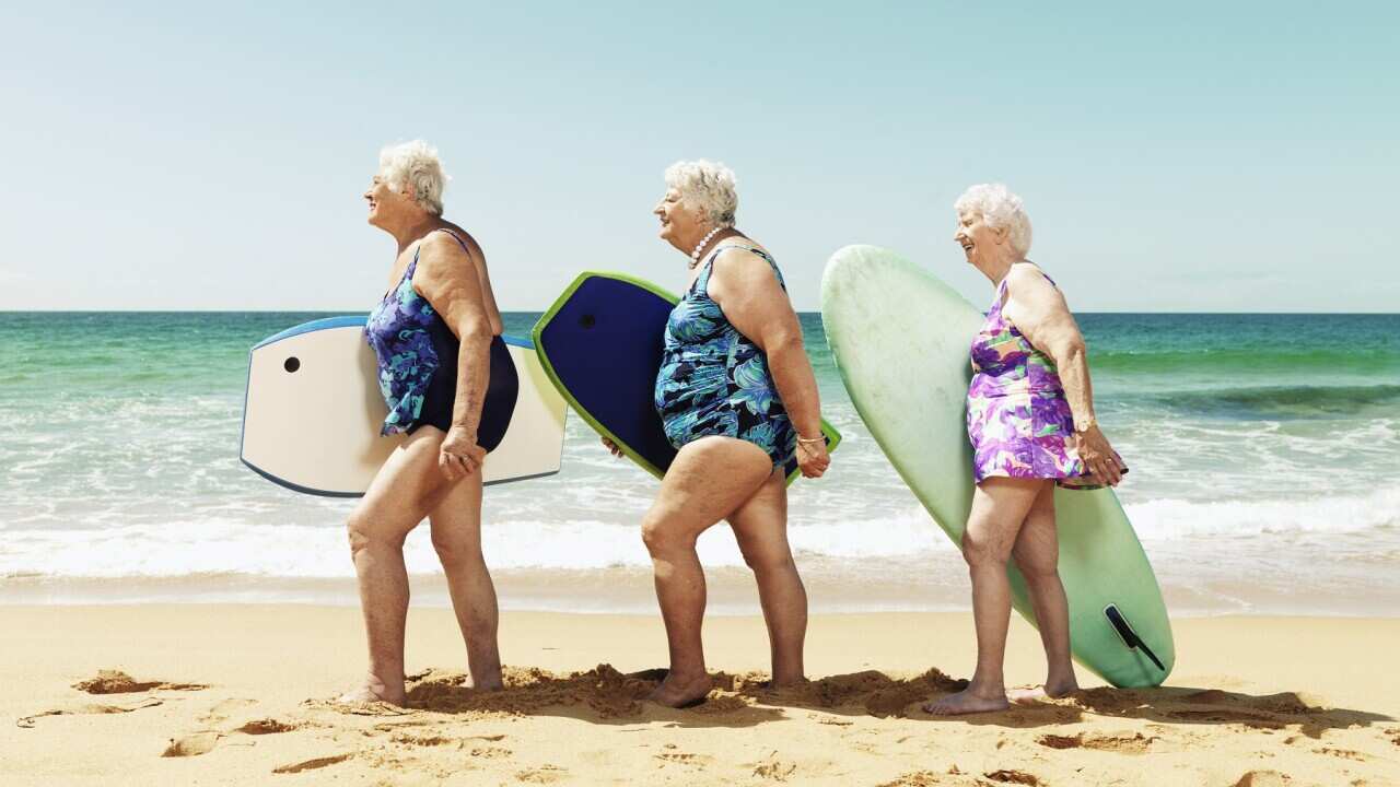 Three mature women on beach with surfboards