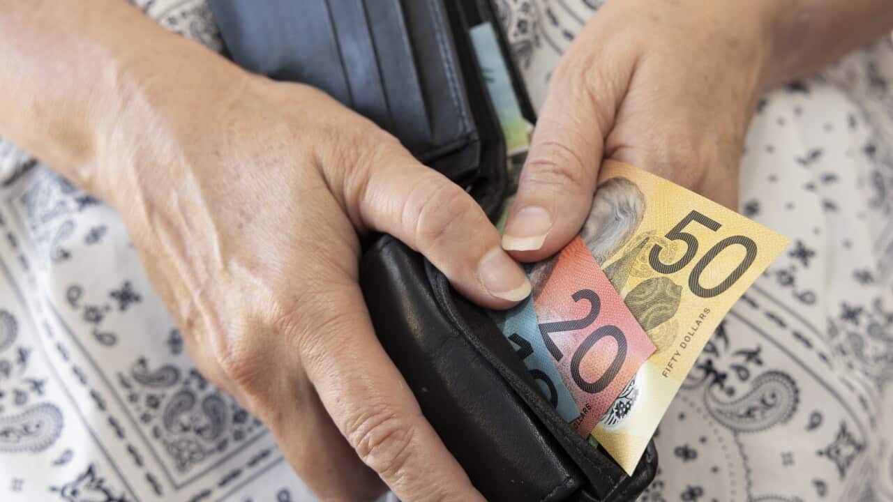 Mature adult holding a wallet containing some Australian bank notes.