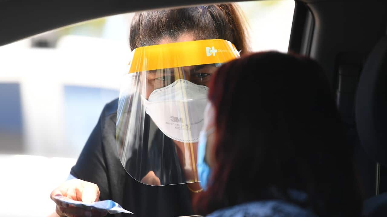 A woman wearing a face shield and face mask gives a rapid antigen test kit to a woman in a car in Melbourne.