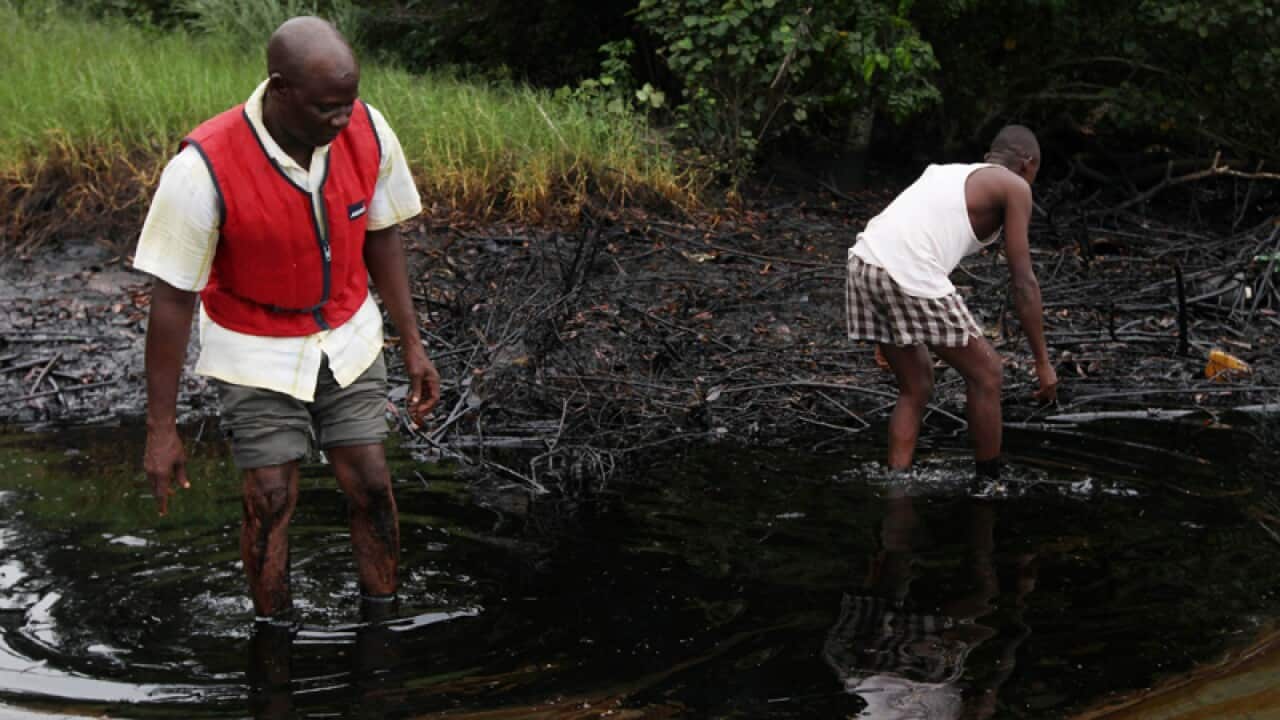 Men walk in an oil slick covering a creek near Bodo City