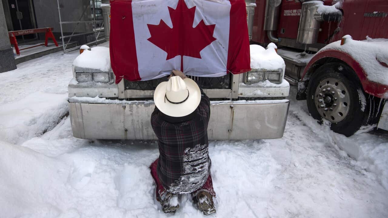 A trucker removes a Canada flag from the hood of their vehicle
