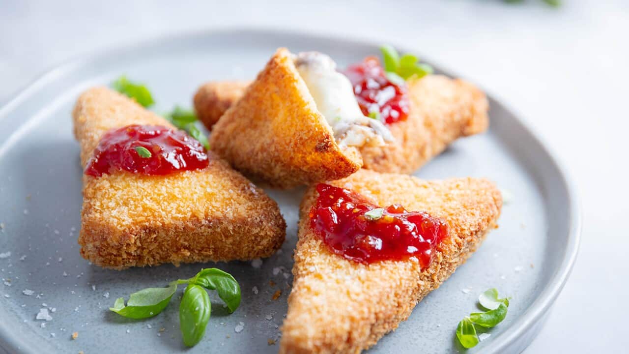 Several crumbed and cooked triangles sit on a plate. One has been cut open, showing the melted cheese inside.