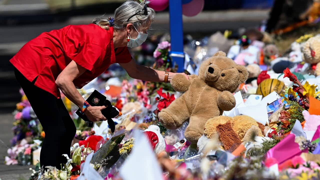 A woman placing a teddy bear at a memorial.