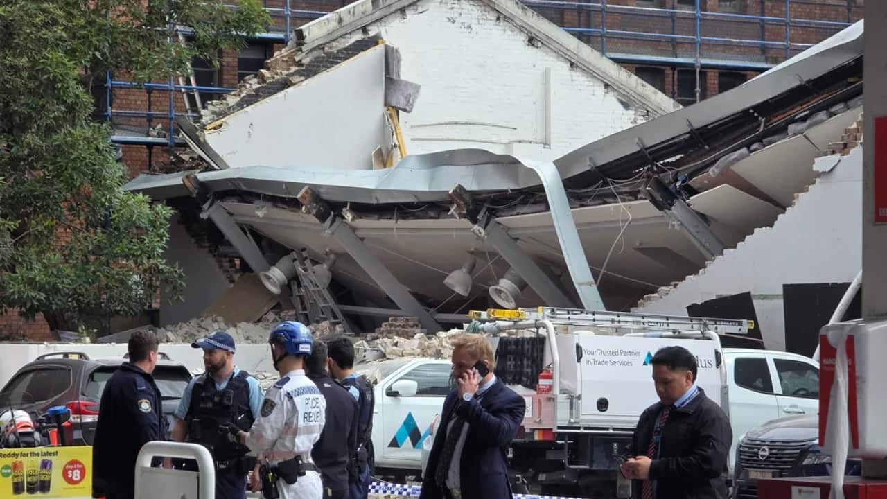 A group of seven uniformed people standing in front of a collapsed roof.