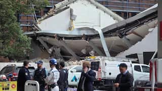 A group of seven uniformed people standing in front of a collapsed roof.