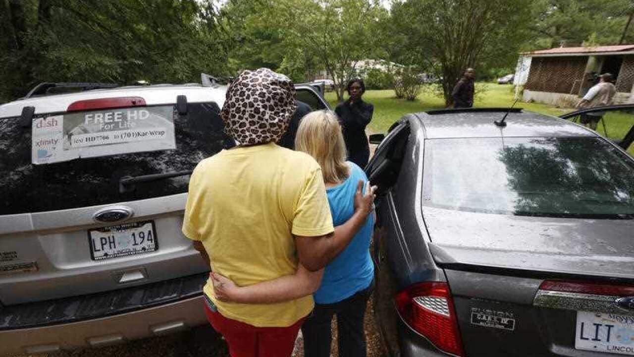 People console each other Sunday, May 28, 2017, near a house, in the background center, where several people were fatally killed Saturday in Mississippi