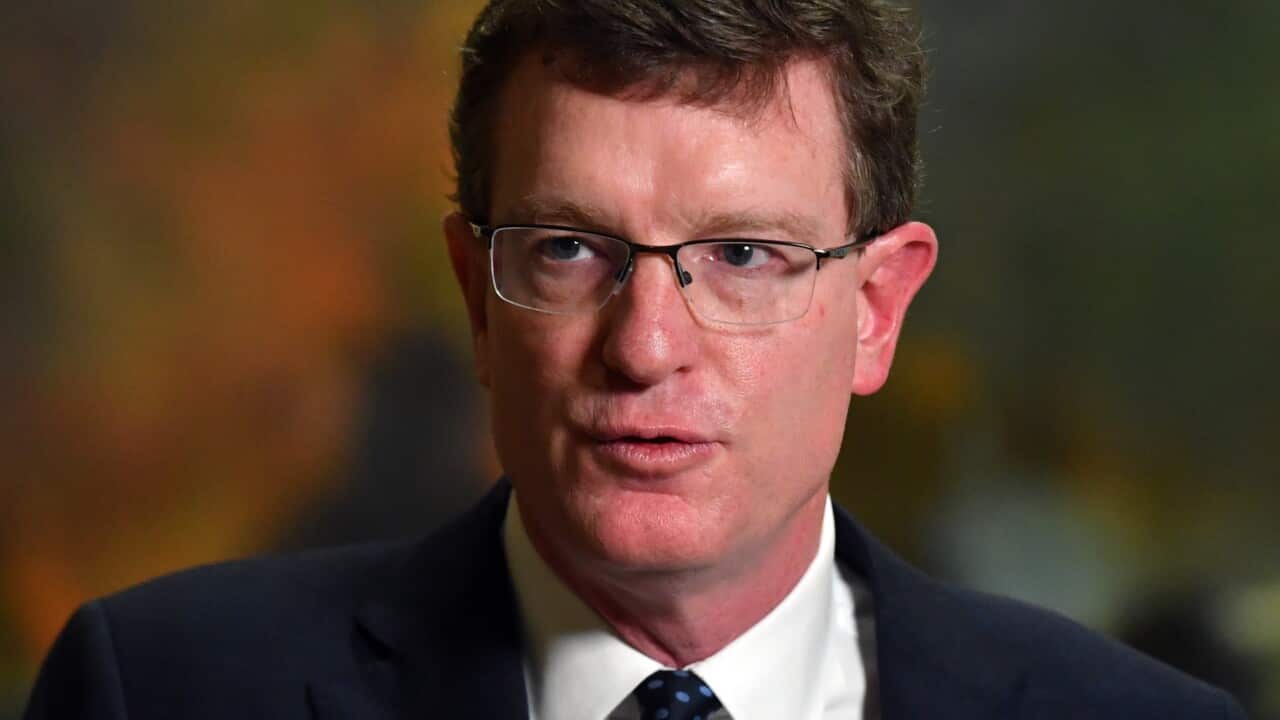 A man wearing a suit, tie, and glasses who is speaking.
