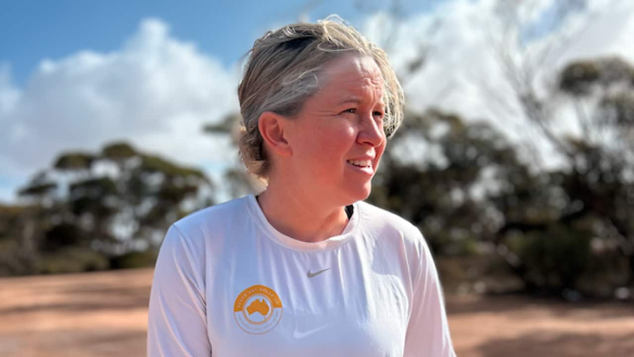 A woman wearing a white top stands in a desert landscape.
