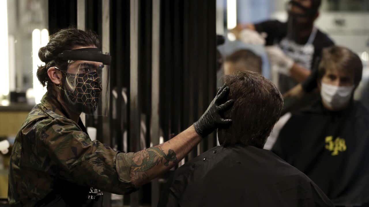 A barber wears a face shield, mask, and gloves for protection amid the COVID-19 pandemic while attending a client on the first day the shop was allowed to reopen, as restrictions ease in Brasilia, Brazil, Wednesday, July 15, 2020. (AP Photo/Eraldo Peres)