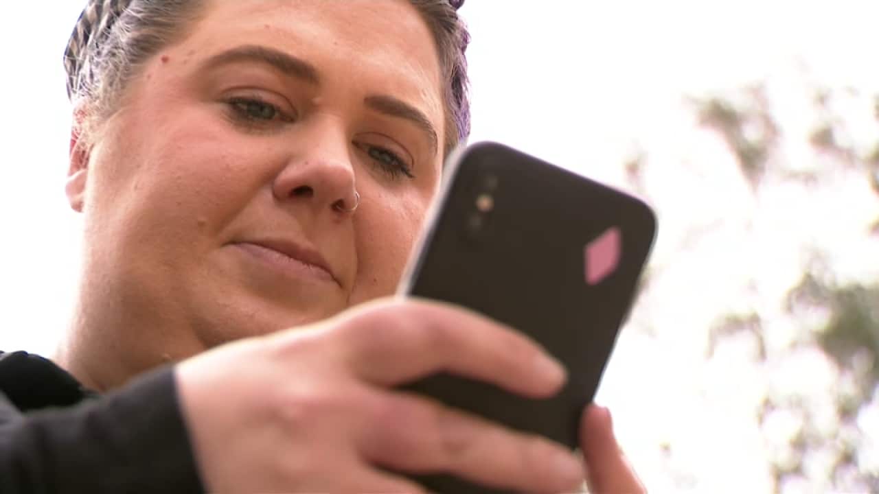 A woman holding a black mobile phone in her hands, looking down at it.