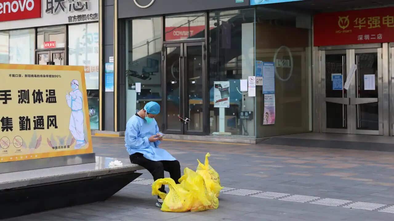 A janitor checks his phone outside closed shops in Huaqiangbei area, the world's biggest electronics market, in Shenzhen in south China's Guangdong province on Monday, 14 March, 2022.